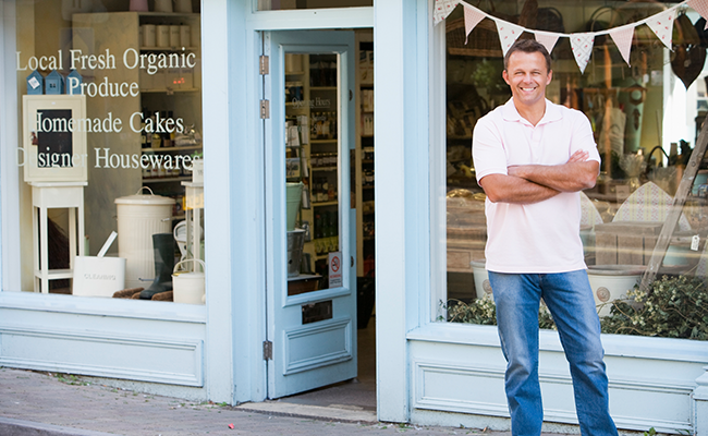Man standing with arms crossed outside a small retail shop