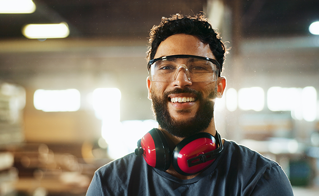 Smiling worker wearing safety glasses and ear protection in an industrial workspace