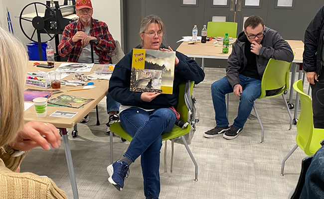 Group discussion during support meeting People seated in a group discussion during a support meeting, with one person holding a book