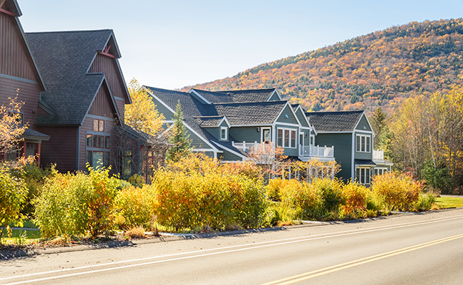 Residential homes along a road with fall foliage and mountains in the background